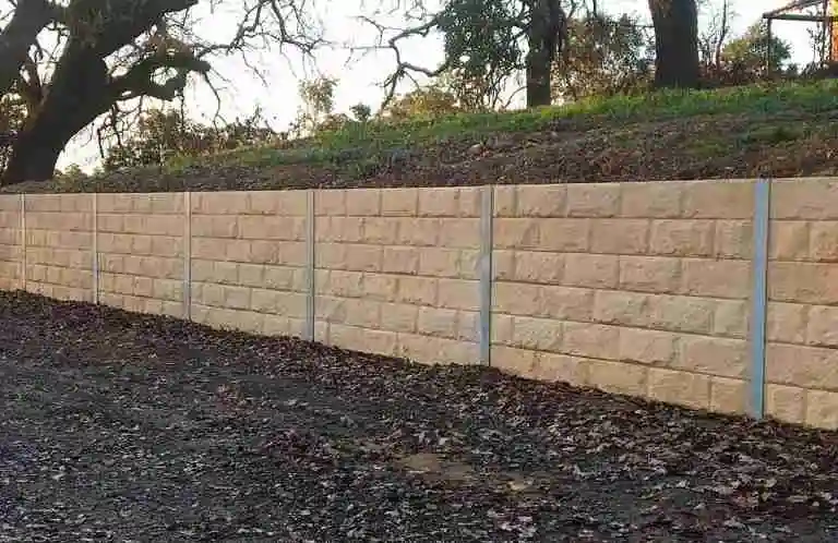 Modern concrete sleeper retaining wall with steel posts supporting a landscaped slope.