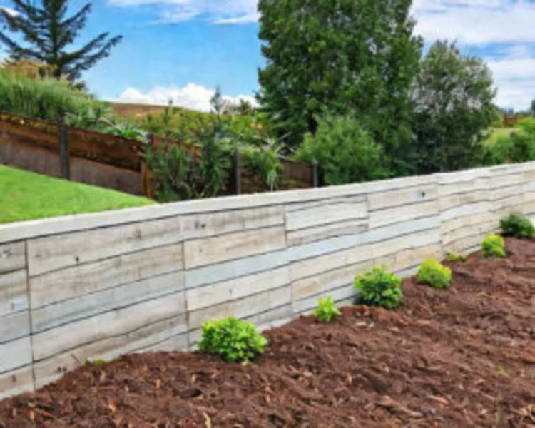 Light-coloured concrete sleeper retaining wall with young plants and garden soil in front.