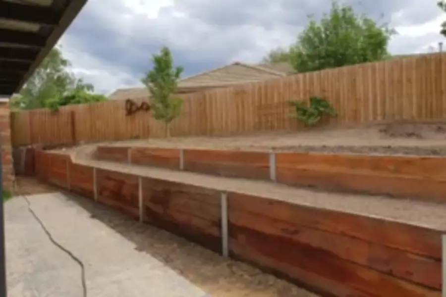 Timber retaining wall sleepers installed along a sloped backyard with a wooden fence.