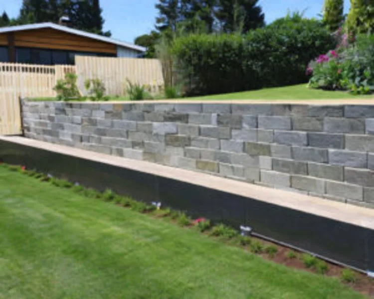 Modern concrete block retaining wall with landscaped garden and timber fence.