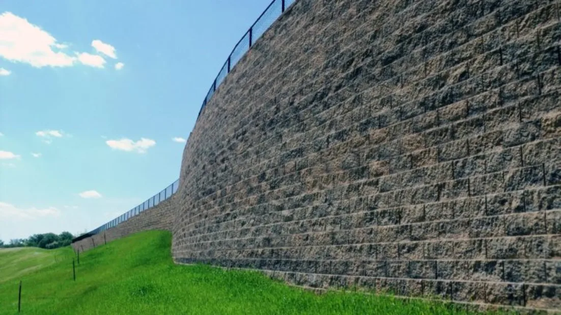 Tall concrete sleeper retaining wall curving along a grassy slope under a blue sky.
