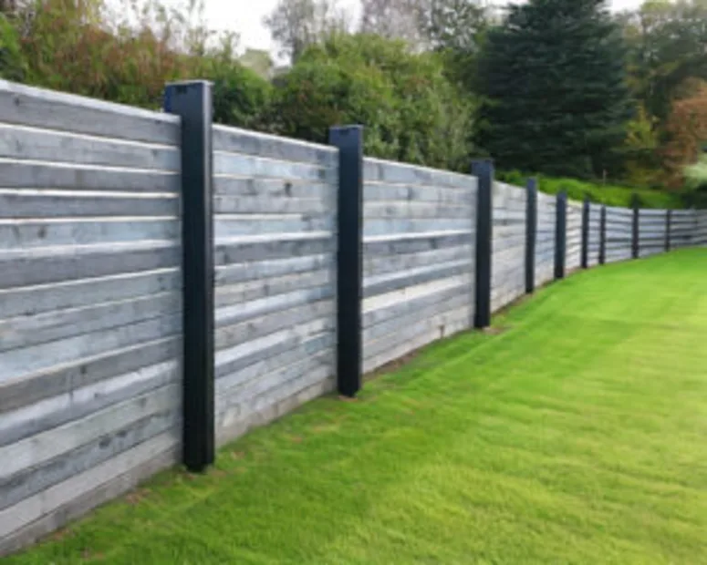 Modern concrete sleeper retaining wall with black steel posts along a green lawn.